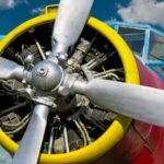 Detailed view of a colorful vintage propeller airplane with a focus on the engine and propellers, set against a blue sky.