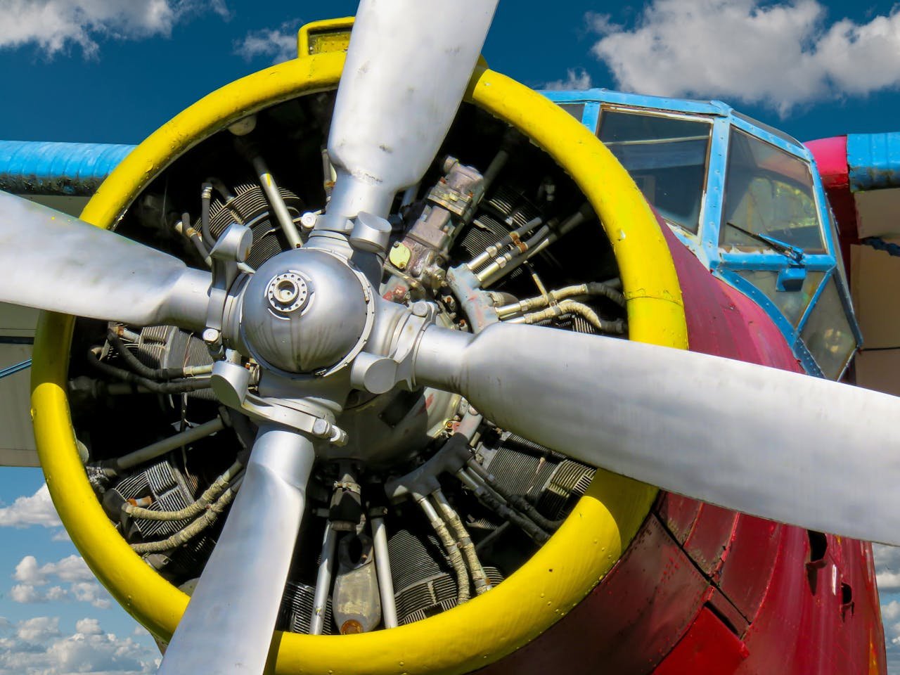 Detailed view of a colorful vintage propeller airplane with a focus on the engine and propellers, set against a blue sky.