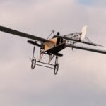 A classic early aircraft, monoplane design, elegantly flies amidst a soft cloudy sky.