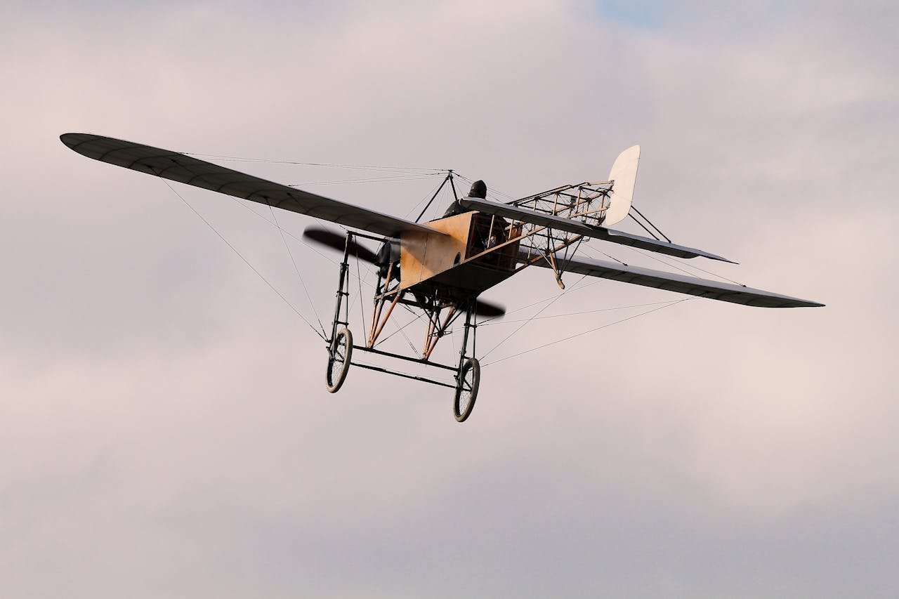 A classic early aircraft, monoplane design, elegantly flies amidst a soft cloudy sky.